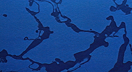 An abstract macro background capturing the organic spread pattern of deep blue ink bleeding onto porous art paper. Shows the unique interaction between the fluid ink and the textured white surface creating artistic detail look.の写真素材