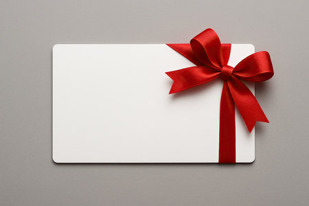 Clean Blank White Gift Card Presentation with Bright Red Ribbon Bow Isolated on Smooth Neutral Grey Backdropの写真素材