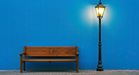 Rustic Wooden Bench Near Illuminated Lamppost Against a Textured Blue Wall at Nightの写真素材