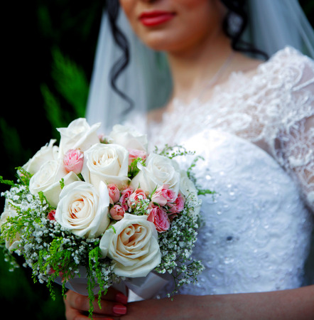 beautiful wedding bouquet of white roses in hands of newlywedsの写真素材