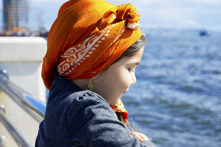 portrait of a pretty little cute girl in a headscarf on the sea, on a background of blue skyの写真素材