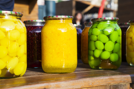 Various canned fruits, Jam and compote of pears, plums, apricots, quinces, cherries,almonds , nuts ,hazelnuts, feijoa and grapes in glass jars on a wooden counter at the fairの写真素材