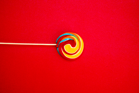 Colorful spiral lollipop candy on stick. On a red background.の写真素材