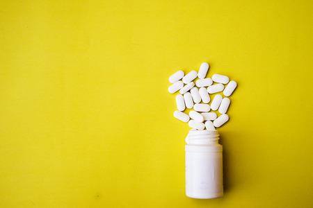 Assorted pharmaceutical medicine pills, tablets and capsules and bottle on yellow background. Top view. Flat lay. Copy space. Medicine concept. Heap of pills on yellow backgroundの写真素材