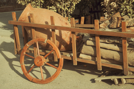 an old wooden cart with a clay jug and firewood stands in the yardの写真素材