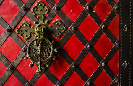 A black forged handle on the iron red door. Old vintage door with iron handle.の写真素材