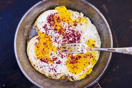 scrambled eggs in an iron skillet on a brown wooden table.