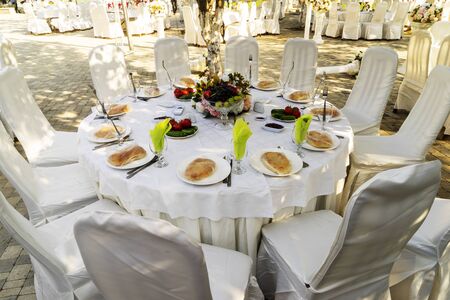 Elegant banquet tables prepared for a conference or a party and covered with a white tablecloth and decorated with flowers for guestsの写真素材