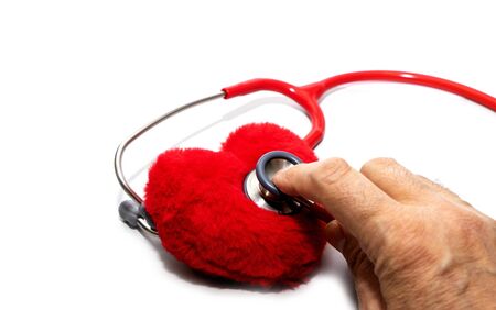 Closeup of man hand holding a red stethoscope on heart - medical diagnostic device for auscultation listening of sounds coming from the heart, bronchi, isolated, blurred heart on white background.の写真素材