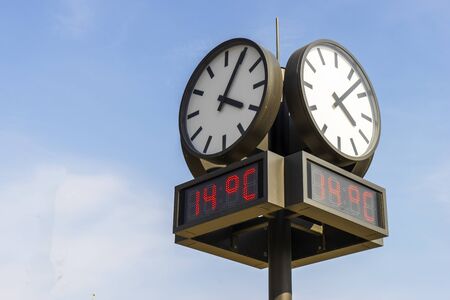 Round outdoor clock with electronic thermometer against the blue sky