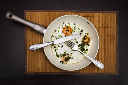 Pan of fried eggs, bacon with heerbs on rustic wood table surface, top view.の写真素材
