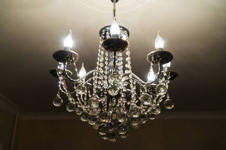 A crystal chandelier with light bulbs hangs from the ceilingの写真素材