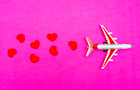 Airplane toy and heart on red, pink background, love travel concept