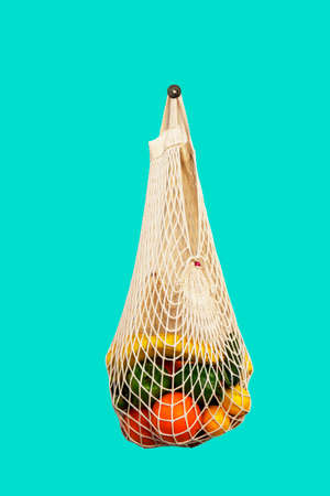 White string bag with different vegetables and fruits on a green background. top view
