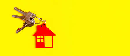 Home key with house keyring or keychain on solid yellow background using as home ownership, mortgage or buy and sell property and real estateの写真素材