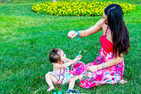 Happy mother and daughter in the park. Beauty nature scene with family outdoor lifestyle. Happy family resting together on the green grass, having fun outdoor. Happiness and harmony in family lifeの写真素材