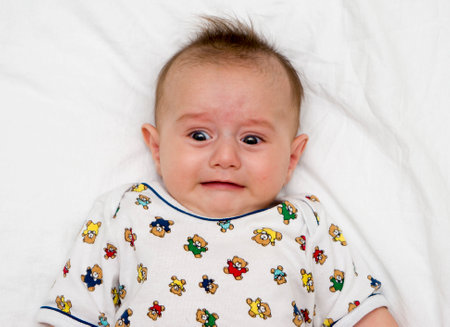 Crying baby lies on a white fluffy backgroundの写真素材