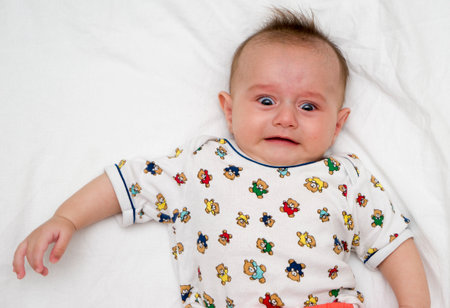 Crying baby lies on a white fluffy backgroundの写真素材