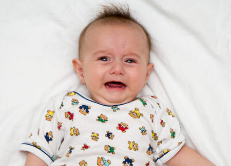 Crying baby lies on a white fluffy backgroundの写真素材