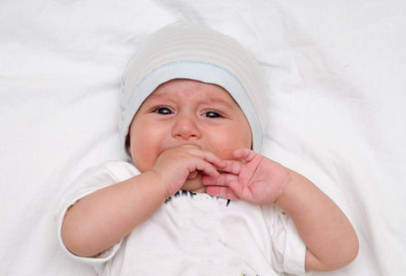 Crying baby lies on a white fluffy backgroundの写真素材