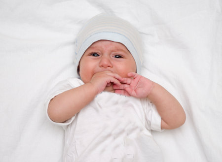 Crying baby lies on a white fluffy backgroundの写真素材