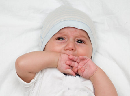 Crying baby lies on a white fluffy backgroundの写真素材