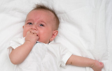 Crying baby lies on a white fluffy backgroundの写真素材