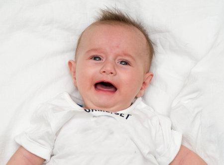 Crying baby lies on a white fluffy backgroundの写真素材