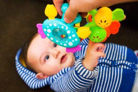 Small cute baby in body lies on his back in crib and holds toy in his hands. selective focusの写真素材