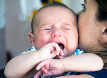 portrait of a newborn baby boy in his mother's shoulder. A newborn baby cries in his mother's armsの写真素材