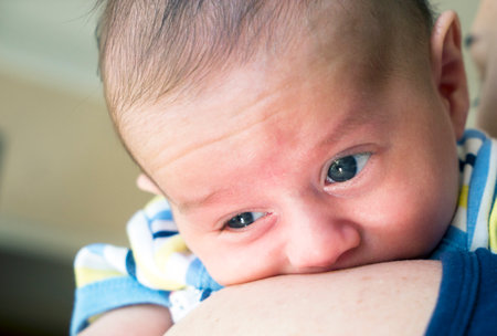Baby little boy with blue eyes held in mother's arms for comfortの写真素材