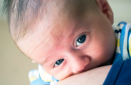 Baby little boy with blue eyes held in mother's arms for comfortの写真素材