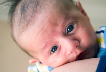 Baby little boy with blue eyes held in mother's arms for comfortの写真素材