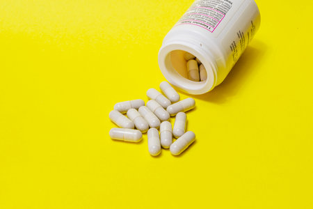 Pills spilled out of white bottle on yellow background. Mock up for special offers as advertising or...