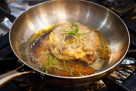 A piece of lamb leg is fried in oil in an iron pan.の写真素材