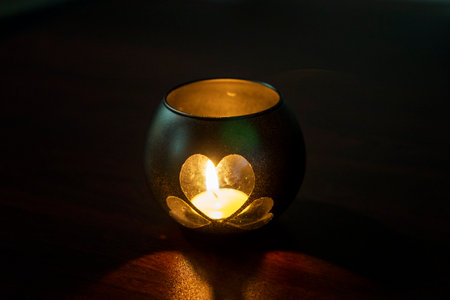 A handmade candle holder. A candle holder made of a glass jar, in the shape of a heart, stands on a table in a dark room. Valentine's Day, decoration, romantic atmosphere.の写真素材