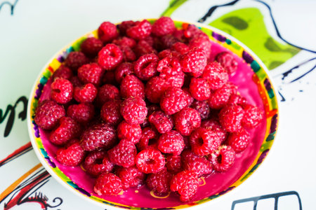 Plate with raspberries on white wooden table. Top view.