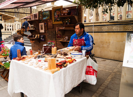 BAKU, AZERBAIJAN - JANUARY 24, 2022: A craftsman sits at a table and prepares souvenirs from wood. A workshop for wood processing or wood carving near the street market. there are many wooden souvenirs and products around it.のeditorial素材