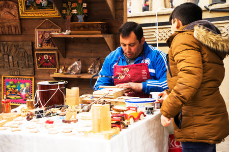 BAKU, AZERBAIJAN - JANUARY 24, 2022: A craftsman sits at a table and prepares souvenirs from wood. A workshop for wood processing or wood carving near the street market. there are many wooden souvenirs and products around it.のeditorial素材