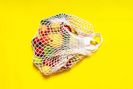 White string bag with different vegetables and fruits on a yellow background. top viewの写真素材