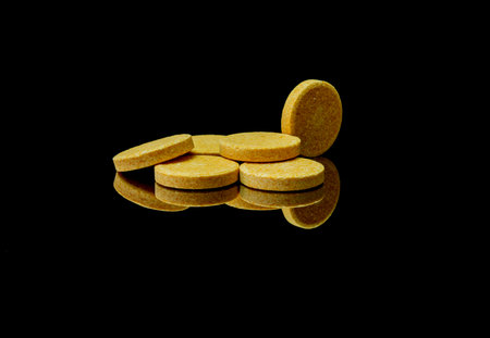 yellow vitamin pills on a black background with reflection