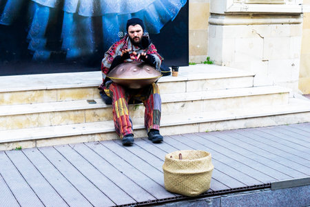 BAKU, AZERBAIJAN - DECEMBER 02, 2023 : A young guy with dreadlocks and a beard plays a percussion musical instrument Hang in the city on the street.のeditorial素材