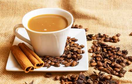 A white cup with a saucer and coffee and coffee beans on a brown cloth background.の写真素材