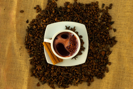 A white cup with a saucer and coffee and coffee beans on a brown cloth background.の写真素材