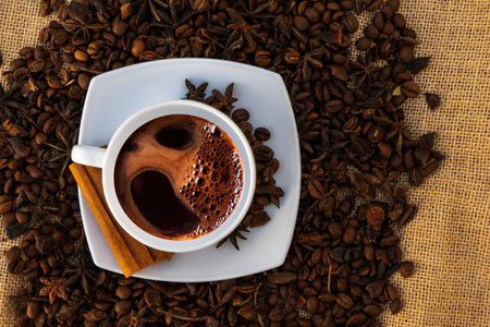 A white cup with a saucer and coffee and coffee beans on a brown cloth background.の写真素材