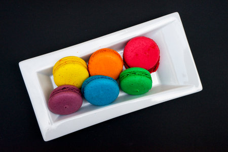 colored macaroons on a white plate on a black backgroundの写真素材