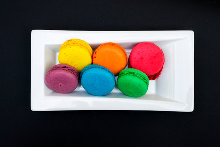 colored macaroons on a white plate on a black backgroundの写真素材