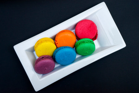 colored macaroons on a white plate on a black backgroundの写真素材