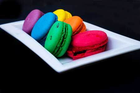 colored macaroons on a white plate on a black backgroundの写真素材