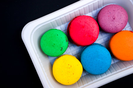 colored macaroons on a white plate on a black backgroundの写真素材